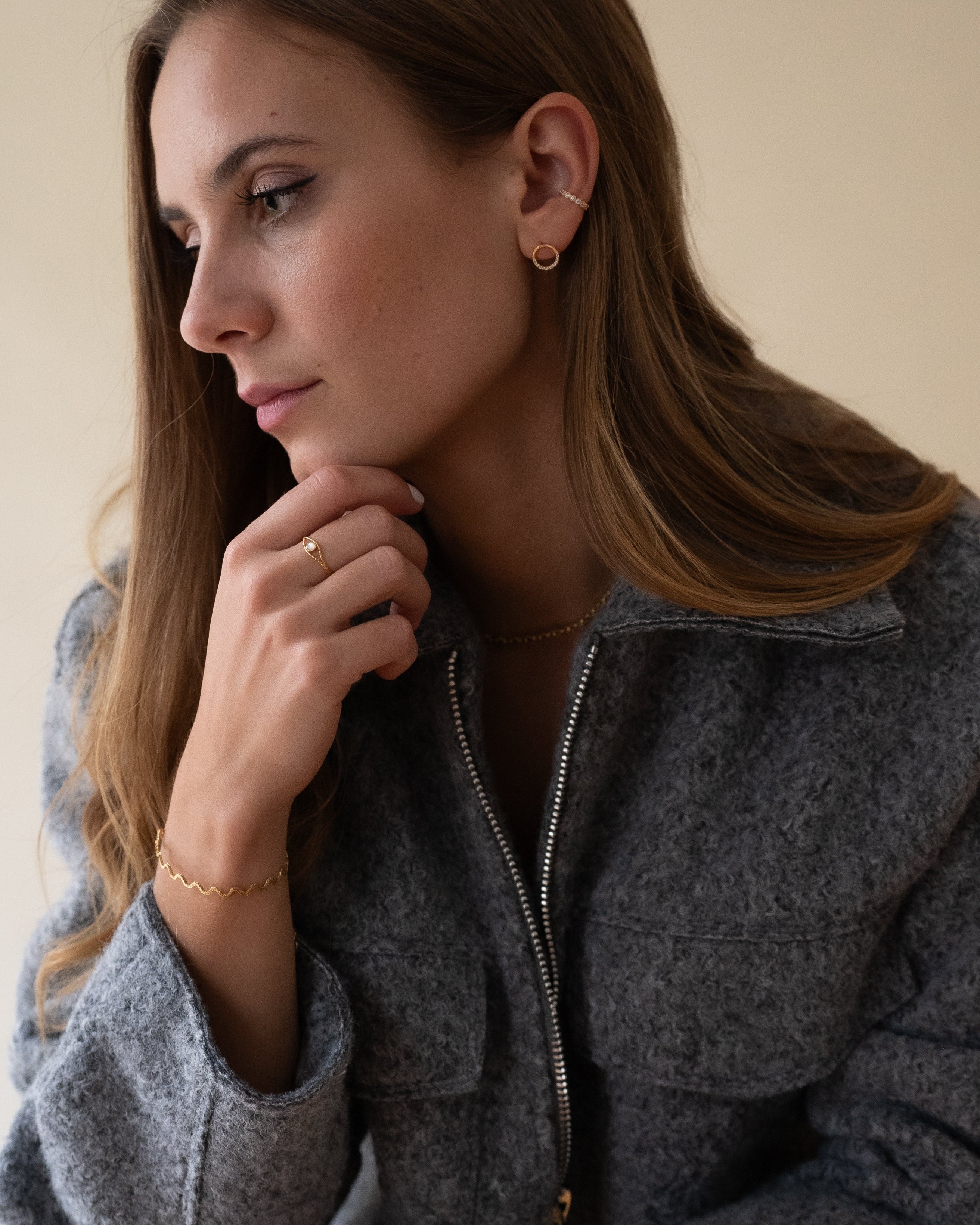 Bijoux en plaqué or, dont un bracelet vague, une bague sertie d'une nacre et des boucles d’oreilles rondes. Accessoires raffinés pour un look chic et moderne.