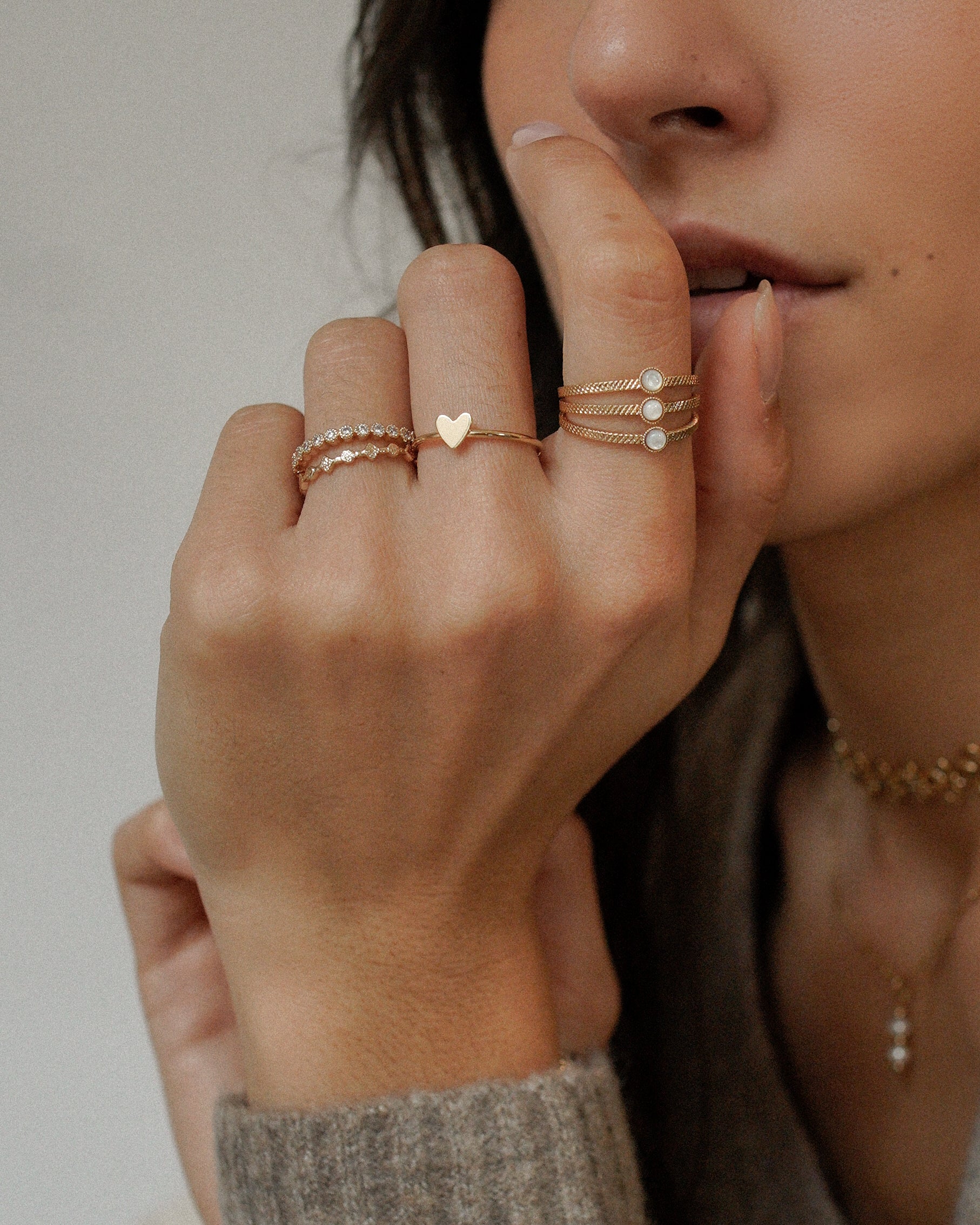 Main féminine ornée de plusieurs bagues en plaqué or, dont une bague fine avec un motif cœur minimaliste. Bijoux élégants et tendance pour un look raffiné et romantique.