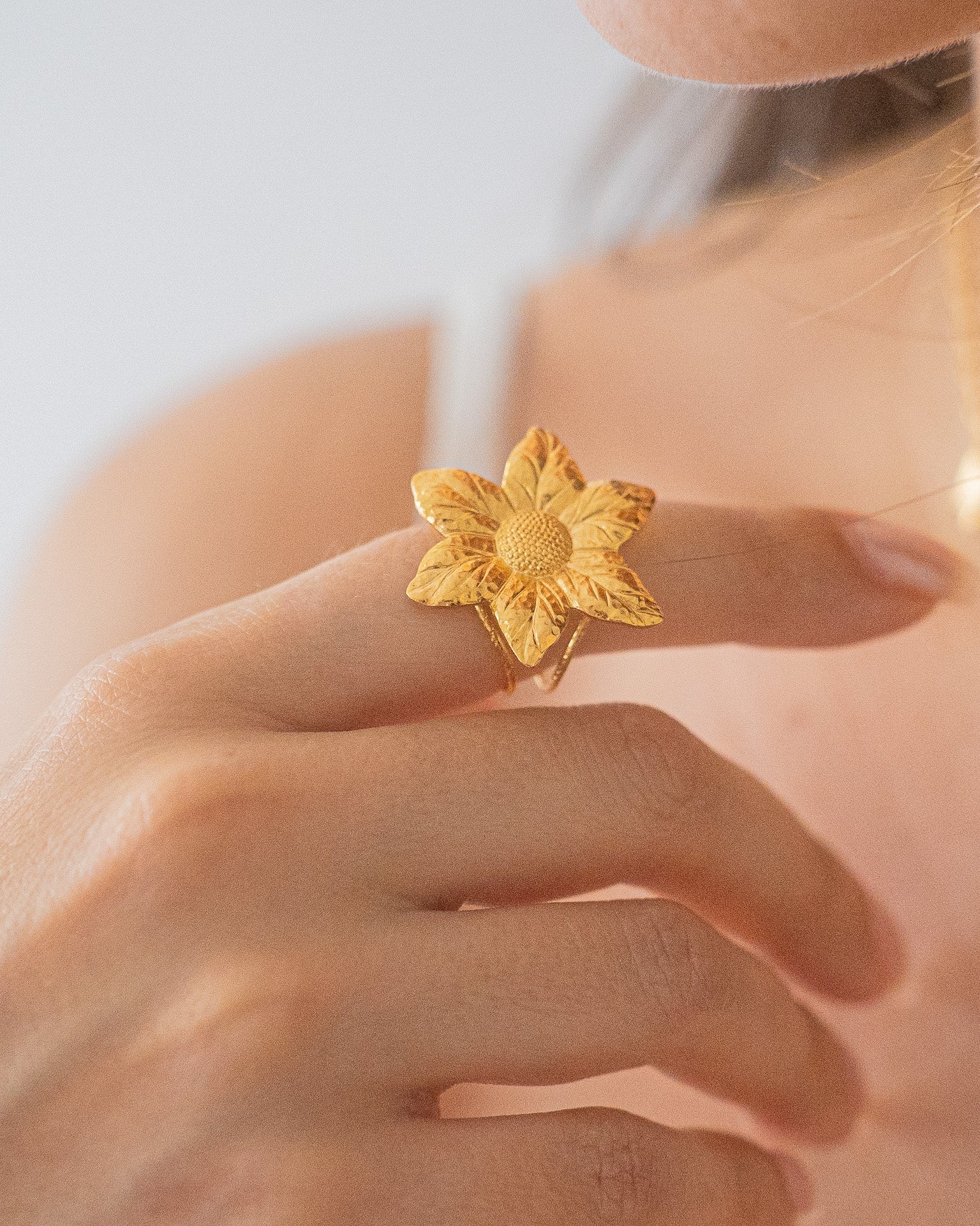 Bague en plaqué or en forme de fleur sculptée, portée sur une main féminine. Bijou élégant et raffiné au design floral détaillé.